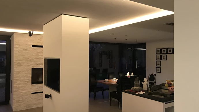 Ein fertiger Wohnraum mit individueller Deckenlösung hat eine maßgeschneiderte Decke mit integrierten Lichtelementen. Der Kamin wurde zusätzlich verkleidet, um eine ansprechende und einzigartige Atmosphäre im Raum zu schaffen.
